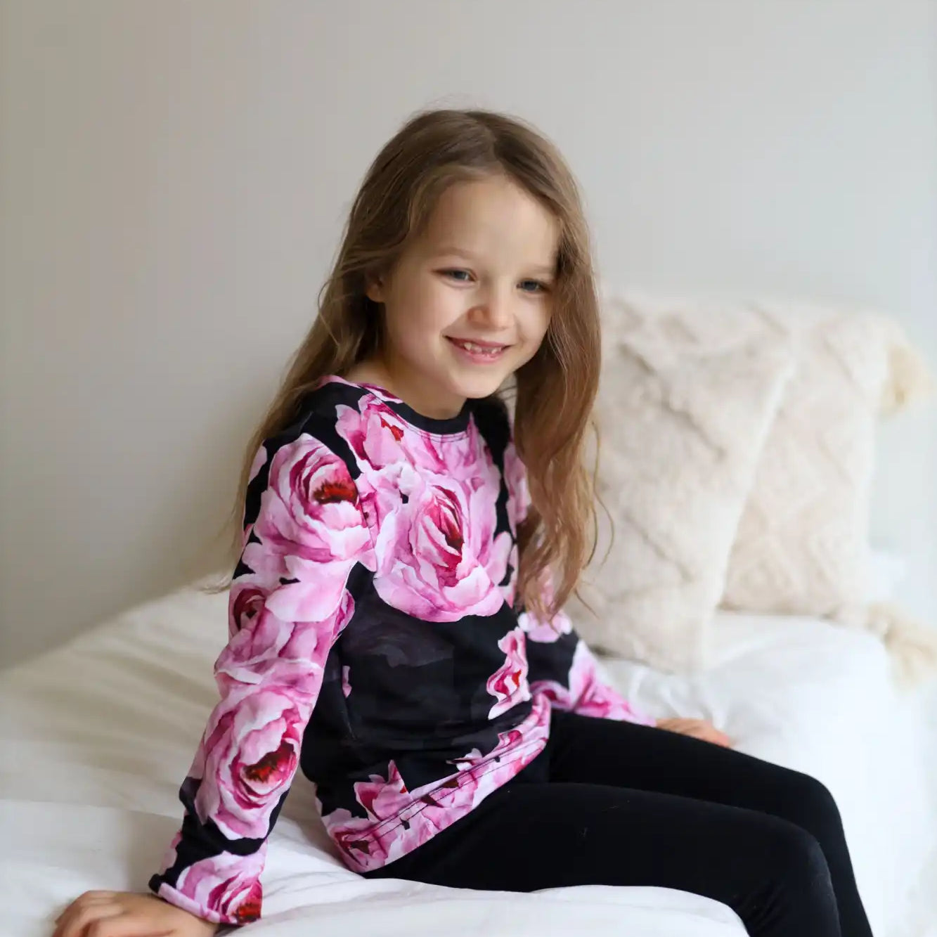 Nuori tyttö, jolla on musta pitkähihaista paitaa, jossa on kirkkaan pinkki ruusukuvio, ja mustat leggingsit.